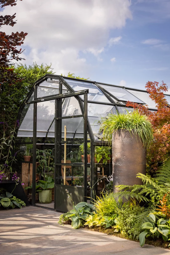 Contemporary glasshouse with lush planting and a tall sculptural planter.