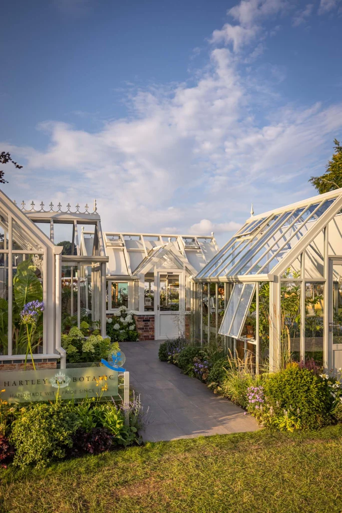 White-framed greenhouses surrounded by soft planting under a blue sky.